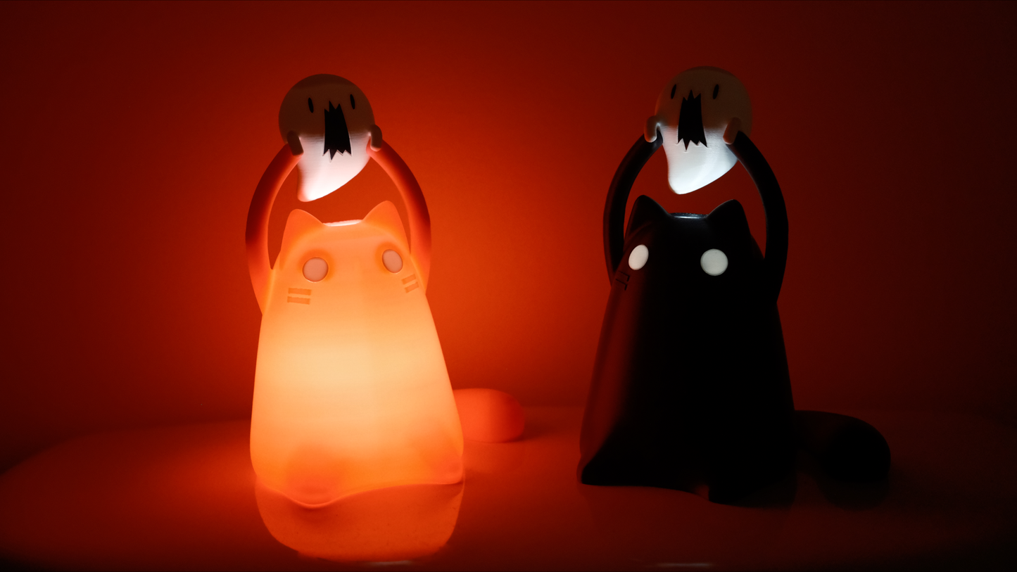 A pink and black cat figurine are shining in the dark and they are each holding mini ghosts above their heads
