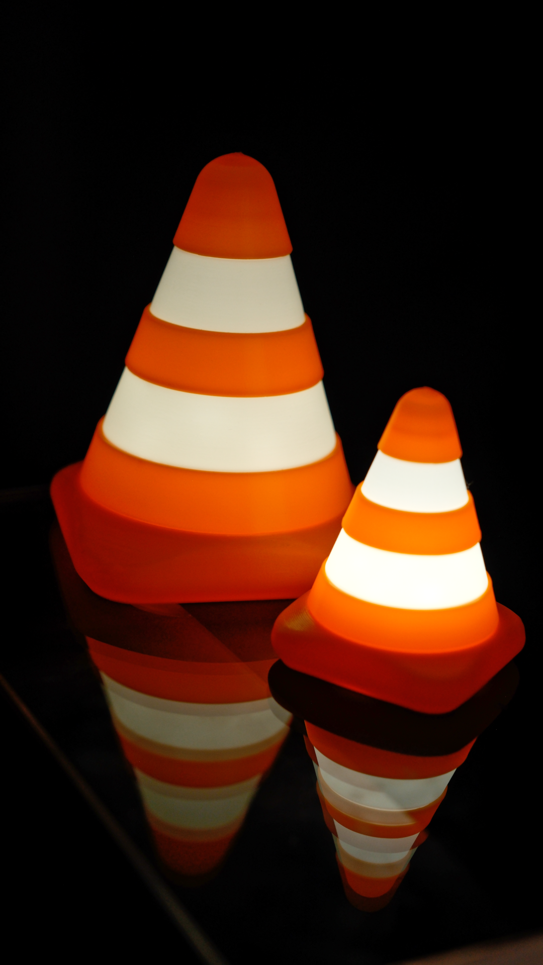 two light up traffic cones on a glass table in the dark