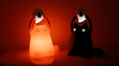 A pink and black cat figurine are shining in the dark and they are each holding mini ghosts above their heads