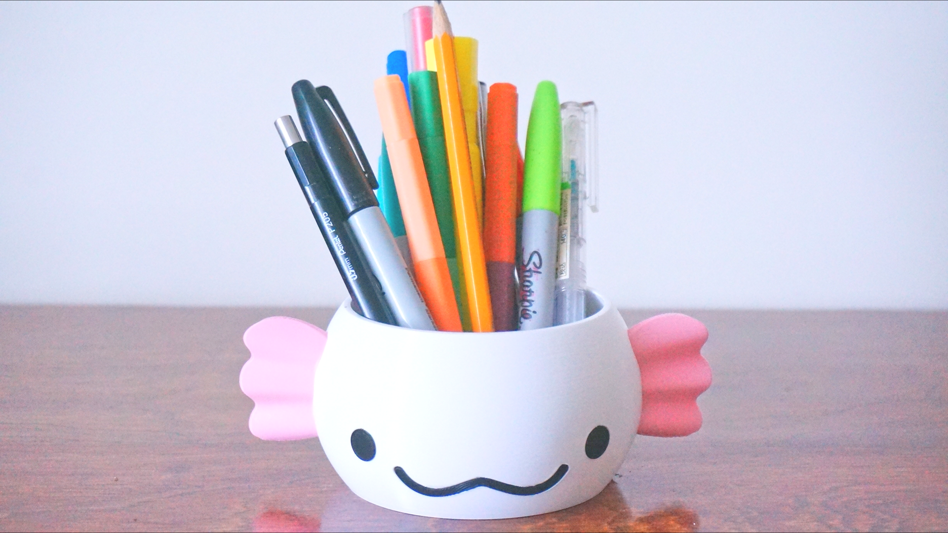 An axolotle shaped planter is holding multicolour pens, pencils, and markers.